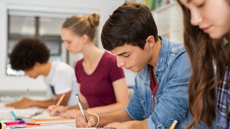 Grupo de estudantes concentrados enquanto realizam uma prova ou atividade acadêmica em uma sala de aula. A imagem representa a preparação para vestibulares e exames, simbolizando o foco e a dedicação necessários para ingressar no ensino superior.