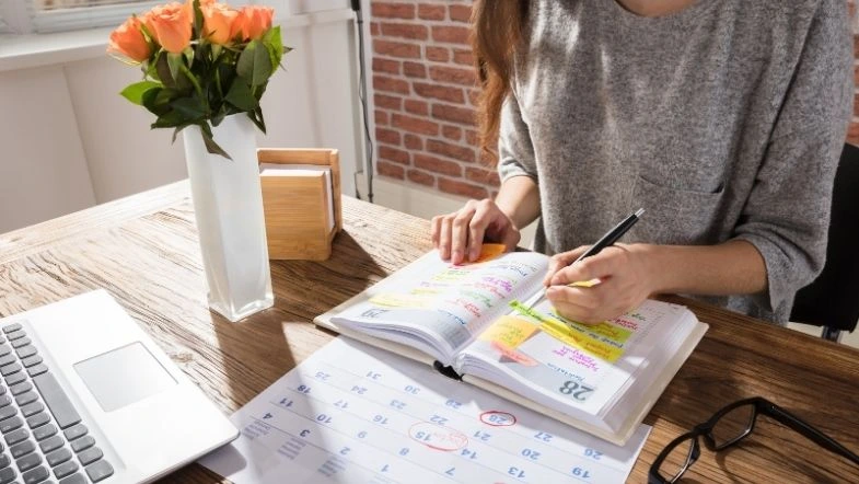 Pessoa organizando seu planejamento em uma agenda, destacando compromissos e prazos. A cena representa gestão do tempo, produtividade e preparação para estudos ou vestibular.