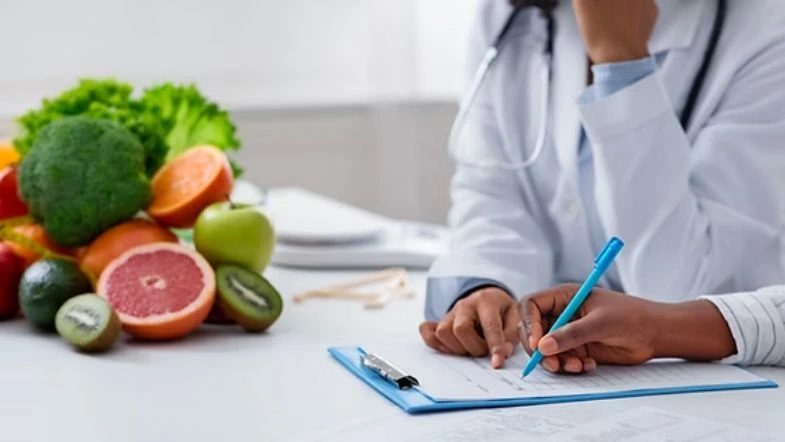 Graduação em Nutrição: o que se estuda, onde o nutricionista pode atuar e por que escolher a Faculdade ITH 7 Profissional da saúde orienta paciente durante consulta nutricional, com prancheta e frutas variadas sobre a mesa, representando avaliação alimentar e planejamento dietético.