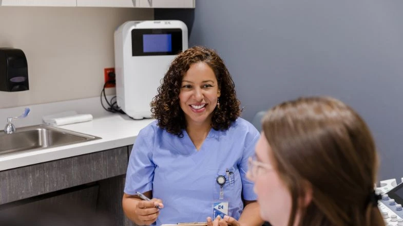 Enfermagem Obstétrica: o enfermeiro e a humanização do parto 8 Enfermeira obstetra sorri enquanto realiza atendimento humanizado a uma gestante em consultório, evidenciando o cuidado, a escuta ativa e a importância da Enfermagem Obstétrica no pré-natal.