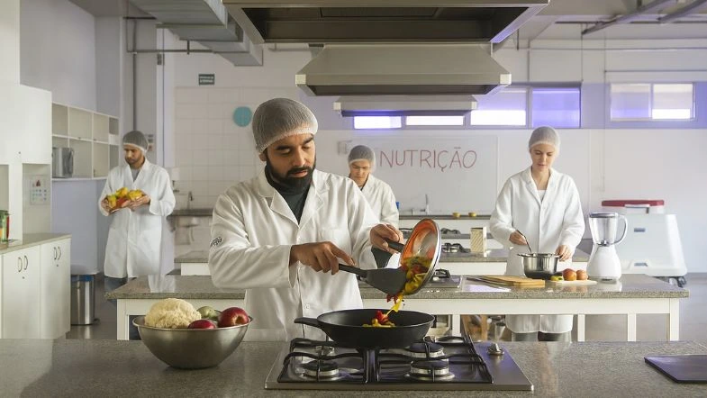 Graduação em Nutrição: o que se estuda, onde o nutricionista pode atuar e por que escolher a Faculdade ITH 9 Estudantes da graduação em Nutrição realizam atividade prática em laboratório de técnica dietética, preparando alimentos com uso de toucas, jalecos e utensílios de cozinha profissional, em ambiente acadêmico moderno.