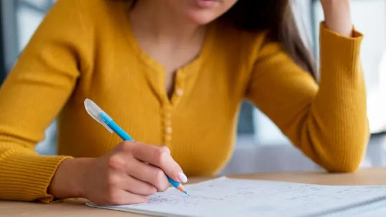ProUni 2025: guia completo com regras, inscrições, requisitos e como garantir sua bolsa 6 Jovem escreve no caderno com caneta azul, concentrada nos estudos, representando preparação para o Enem ou processo seletivo.