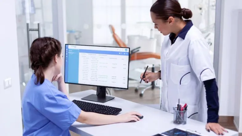Auditoria em Serviços de Saúde: alavanque sua carreira 6 Duas profissionais da saúde analisando dados de pacientes em um computador em ambiente clínico.