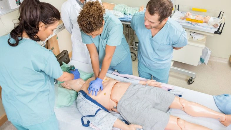 Graduação em Enfermagem: quanto tempo dura, o que se aprende e onde atuar depois de formado? 6 Estudantes de Enfermagem praticam manobras de reanimação cardiopulmonar (RCP) em um boneco de simulação realística em ambiente hospitalar. A cena representa uma aula prática com supervisão, evidenciando o uso de metodologias ativas na graduação em enfermagem.