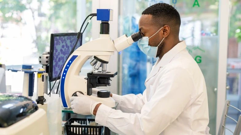 Biomedicina: avanços tecnológicos na saúde 7 Biomédico utilizando microscópio em laboratório moderno, com máscara e jaleco, simbolizando a atuação técnica e analítica na saúde contemporânea.