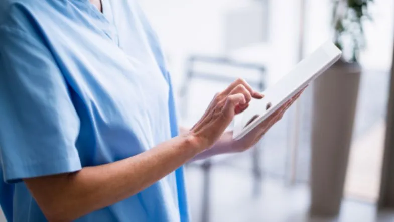 MBA em Qualidade e Acreditação em Saúde: domine ONA, JCI e ISO 7 Profissional de saúde utiliza tablet para registrar ou acessar informações clínicas em ambiente hospitalar.
