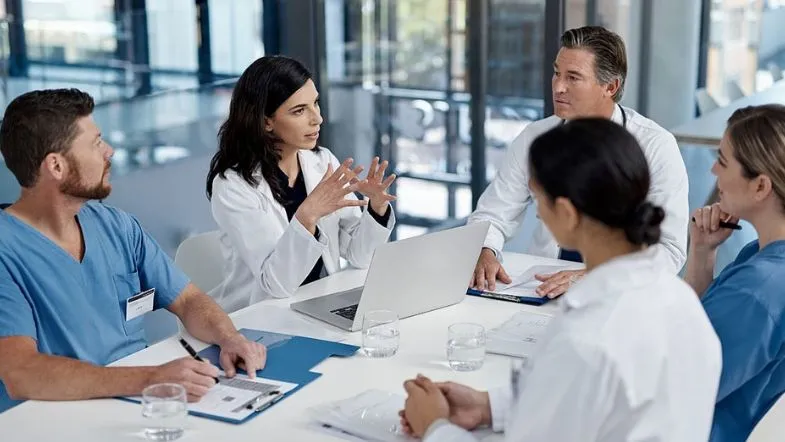 Compliance em Saúde: o que é e quanto ganha esse profissional 7 Profissional de enfermagem conduzindo reunião com equipe multiprofissional da saúde, discutindo estratégias de gestão e compliance.