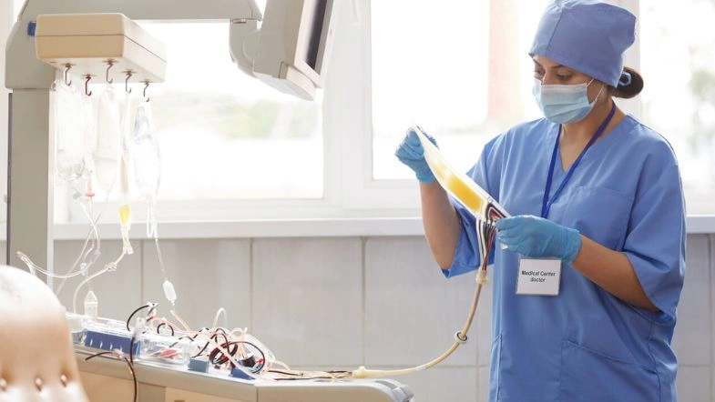 Graduação em Enfermagem: quanto tempo dura, o que se aprende e onde atuar depois de formado? 7 Profissional de Enfermagem manuseia bolsa de sangue em uma clínica de hemoterapia, utilizando equipamentos modernos e seguindo protocolos de biossegurança. A imagem destaca a atuação técnica e cuidadosa do enfermeiro em procedimentos relacionados à transfusão e hemodiálise.
