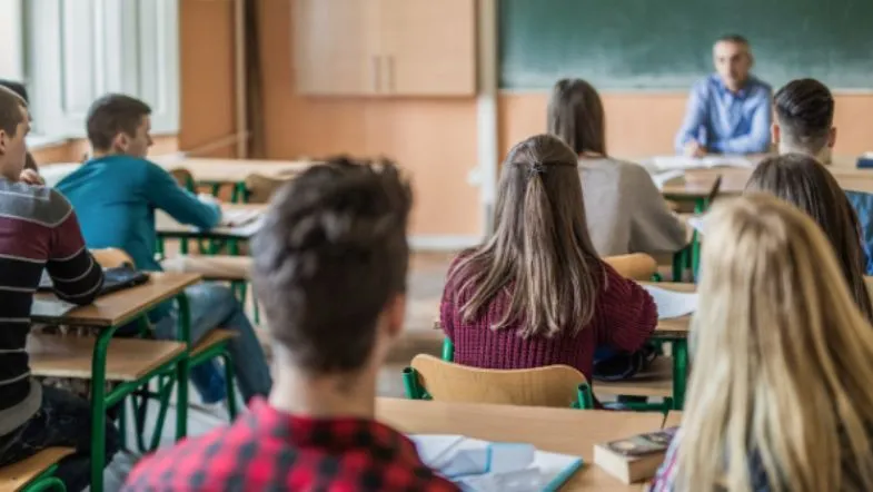 Enem: o que é, como funciona, quem pode fazer e como usar no Sisu, Prouni e outros programas 8 Estudantes sentados em sala de aula prestam atenção ao professor diante do quadro, em ambiente educacional tradicional.