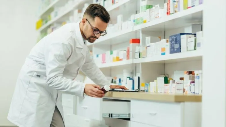 Pós-Graduação em Farmácia Clínica e Atenção Farmacêutica: transforme sua prática profissional 8 Farmacêutico organizando medicamentos em prateleira, representando rotina técnica, controle de estoque e atuação em farmácia comunitária.