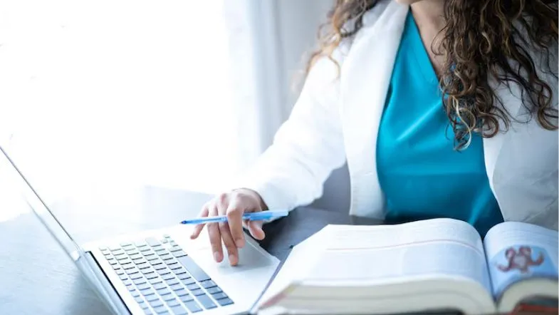 Auditoria em Serviços de Saúde: alavanque sua carreira 8 Profissional da saúde estudando com laptop e livro abertos sobre a mesa, indicando capacitação contínua.
