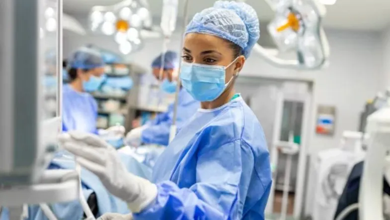 UTI na prática: tudo sobre salário e perfil do enfermeiro intensivista 8 Profissional de enfermagem monitorando sinais vitais e parâmetros clínicos em painel eletrônico durante procedimento em ambiente de terapia intensiva.