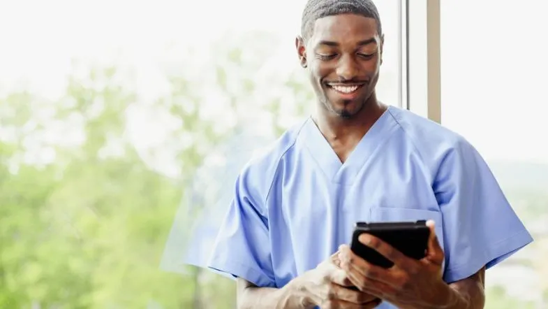 Compliance em Saúde: o que é e quanto ganha esse profissional 8 Profissional da enfermagem sorrindo enquanto visualiza dados em tablet, simbolizando inovação e uso de tecnologia na área assistencial.