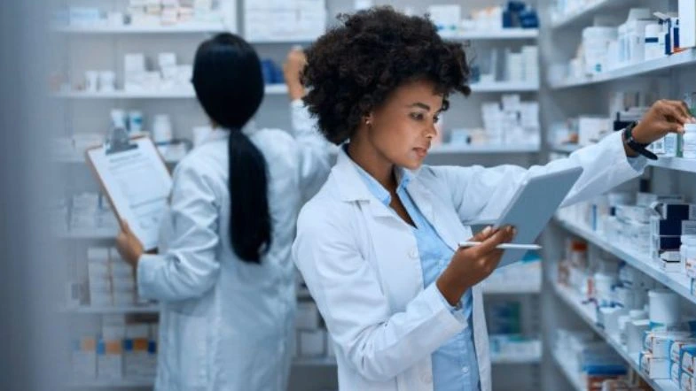 Farmácia: o que faz um farmacêutico, onde atuar e como se destacar na área da saúde 8 Duas farmacêuticas trabalham em uma farmácia, organizando medicamentos e utilizando um tablet para conferência de estoque e informações técnicas.