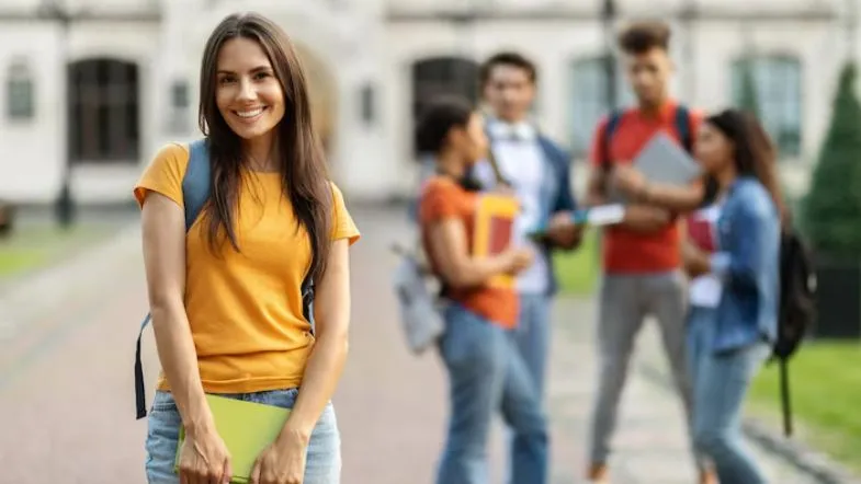 ProUni 2025: guia completo com regras, inscrições, requisitos e como garantir sua bolsa 9 Estudante universitária sorri ao ar livre com caderno na mão, com colegas ao fundo, representando ingresso no ensino superior.