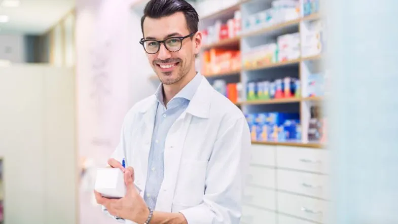 Pós-Graduação em Farmácia Clínica e Atenção Farmacêutica: transforme sua prática profissional 9 Farmacêutico sorrindo e segurando medicamento, simbolizando segurança, atenção farmacêutica e orientação ao paciente.
