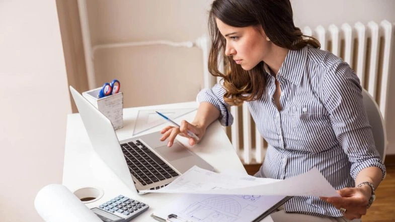 Ciências Contábeis: a profissão que conecta números e propósito 9 Profissional analisa documentos e trabalha no computador, representando a atuação dinâmica em Ciências Contábeis e análise financeira.