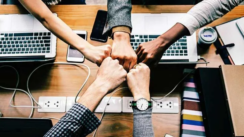 Alta Performance: desenvolva seu potencial e supere seus limites 9 Equipe reunida em gesto de união com punhos juntos sobre mesa com notebooks, simbolizando colaboração, engajamento e espírito de equipe.