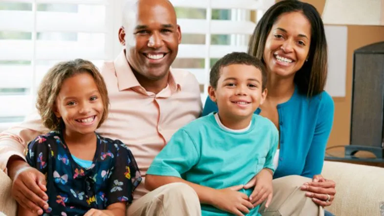 Pós-Graduação em Saúde Coletiva e Saúde da Família: transforme sua carreira 6 Família composta por dois adultos e duas crianças sorrindo em casa, simbolizando o impacto positivo da atuação em saúde da família no bem-estar das comunidades.