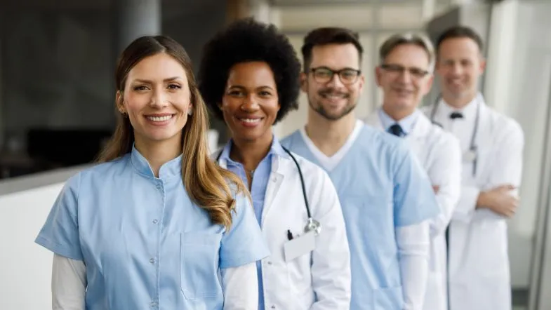 Pós-graduação em Gestão e Metodologia ONA: liderando com excelência 6 Equipe multidisciplinar da área da saúde sorrindo, simbolizando diversidade, trabalho em equipe e formação profissional de alto nível em ambiente clínico.