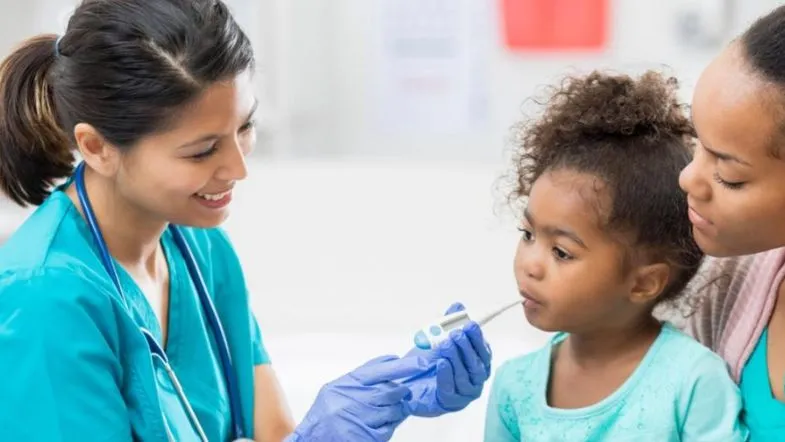 Pós-Graduação em Saúde Coletiva e Saúde da Família: transforme sua carreira 7 Enfermeira examinando menina com a presença da mãe, ilustrando cuidados primários humanizados na Estratégia Saúde da Família.