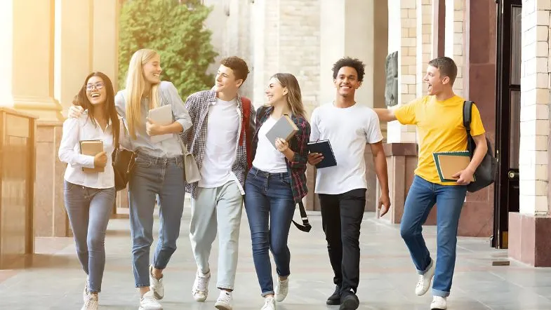 Graduação aumenta em até 57% o salário no brasil: veja como começar a sua 7 Grupo de estudantes universitários sorrindo enquanto caminham no campus da faculdade, simbolizando integração e vida acadêmica.