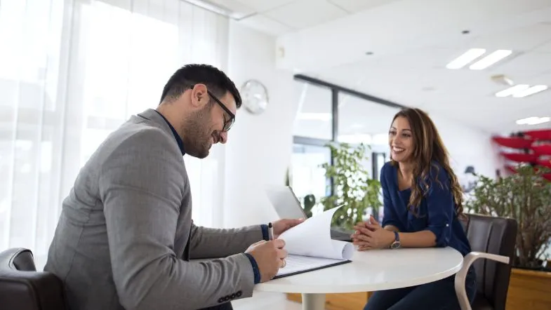 Graduação em Recursos Humanos: guia completo para impulsionar resultados 7 Entrevista de recrutamento entre homem de terno e mulher sorridente em ambiente corporativo iluminado.