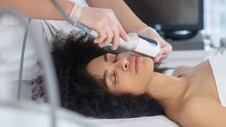 Procedimento estético facial sendo realizado em mulher de pele negra com aparelho não invasivo em consultório estético.