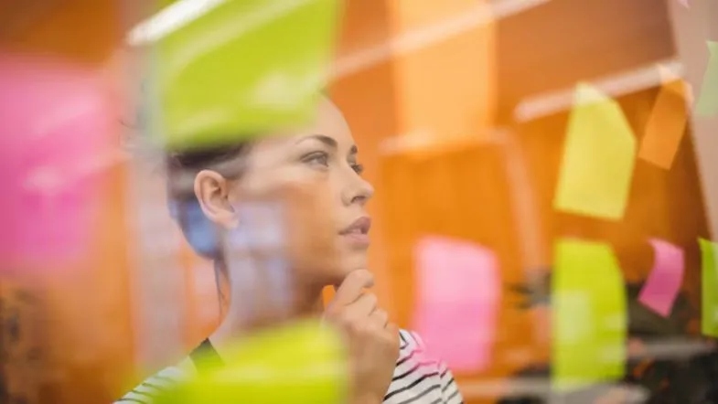 Faculdade ITH realiza masterclass gratuita sobre produtividade, foco e resultados reais 6 Profissional analisando tarefas e planejamentos com post-its coloridos em painel de vidro, representando organização e foco.