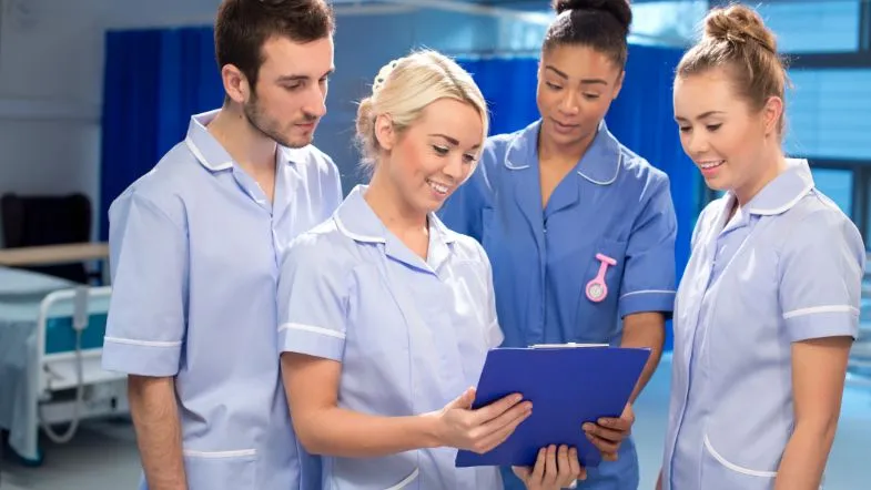 Pós-graduação em Gestão e Metodologia ONA: liderando com excelência 7 Grupo de estudantes ou profissionais da enfermagem analisando prontuário em hospital, representando aprendizado prático, colaboração e formação técnica.