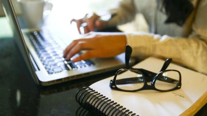 Ensino EAD: saiba quais cursos não podem ser 100% a distância segundo o MEC 7 Mãos digitando em notebook ao lado de caderno e óculos, representando estudo a distância em ambiente doméstico.
