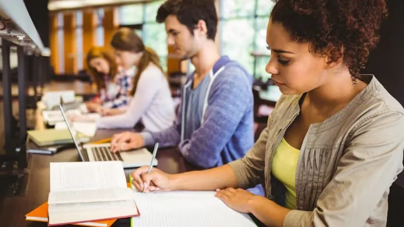 Ensino superior em 2025: saiba como ingressar na faculdade com segurança 8 Grupo de universitários estuda em biblioteca moderna, representando dedicação e foco na vida acadêmica.