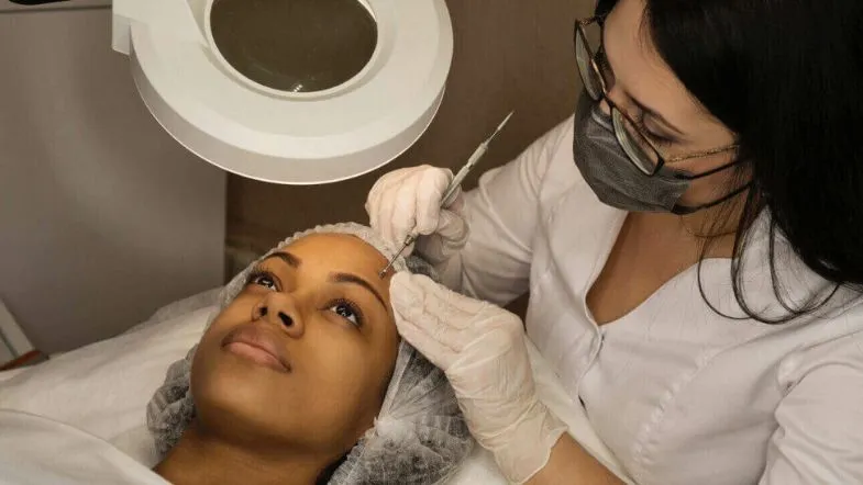 Aplicação de técnica estética avançada na região das sobrancelhas por profissional com equipamento de precisão.