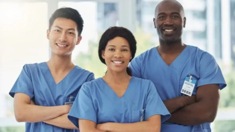 Pós-Graduação em Saúde Coletiva e Saúde da Família: transforme sua carreira 9 Três profissionais da saúde com jalecos azuis e crachás, reforçando o trabalho em equipe e a diversidade na atuação em saúde pública e da família.