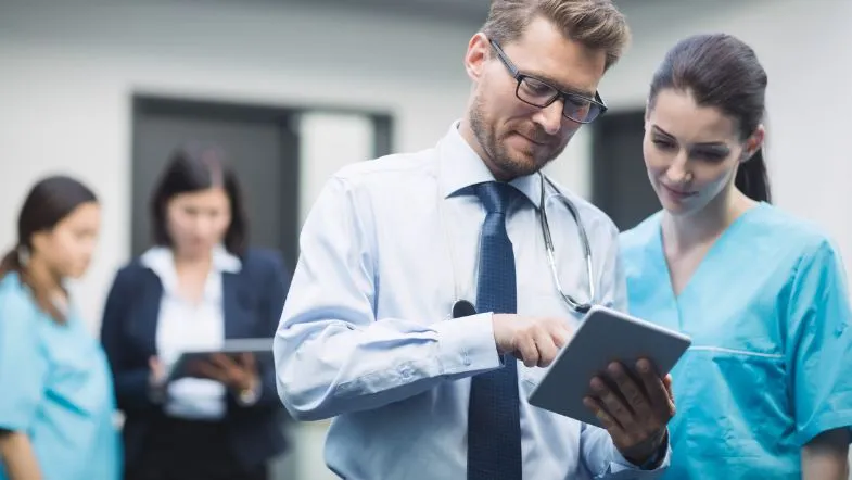 Gestão Hospitalar: transforme seu futuro na saúde e se destaque 9 Médico e enfermeira analisando dados em tablet, destacando a integração entre gestão e assistência na rotina hospitalar.
