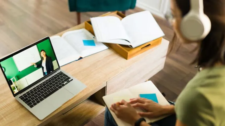 Curso híbrido ou EAD? Veja as diferenças e qual é melhor para você 9 Aluna acompanha aula síncrona pelo notebook com material de estudo aberto, simbolizando o suporte contínuo do ambiente digital no curso híbrido.