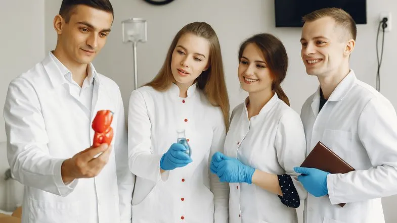 Graduação em saúde: escolha certa para uma carreira de sucesso 9 Quatro estudantes observam um modelo anatômico em aula prática, usando jalecos e luvas, com clima de aprendizado coletivo.