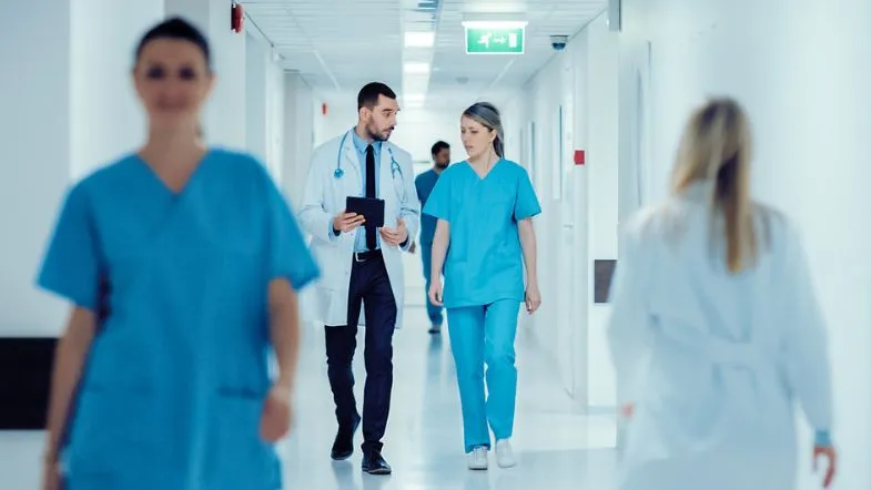 Segurança do Paciente e Qualidade: sua pós com reconhecimento 9 Enfermeiras em uniforme azul reunidas discutindo protocolos de segurança e qualidade assistencial em ambiente hospitalar.