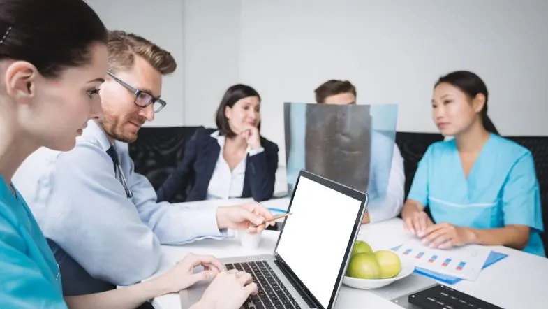 Gestão em Saúde: como o MBA transforma carreiras na área 6 Equipe de médicos e gestores reunidos em uma sala de reunião, analisando gráficos e dados no notebook, representando planejamento estratégico na saúde.