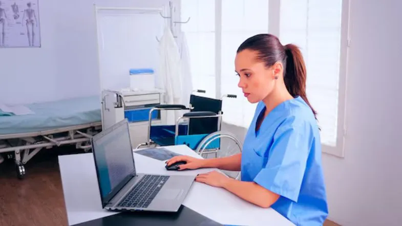Quais áreas de pós-graduação em Enfermagem estão em alta? Confira as mais requisitadas 6 Enfermeira com máscara cirúrgica segurando uma prancheta, ao fundo colegas médicos e enfermeiros revisam documentos, em ambiente hospitalar, representando as diversas áreas que o profissional com pós-graduação em enfermagem pode atuar.