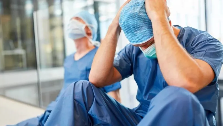 Comunicação ineficaz e a cultura do silêncio nas equipes de saúde: impactos e soluções 6 Profissionais da saúde sentados no chão de hospital, demonstrando sinais de estresse e exaustão mental.