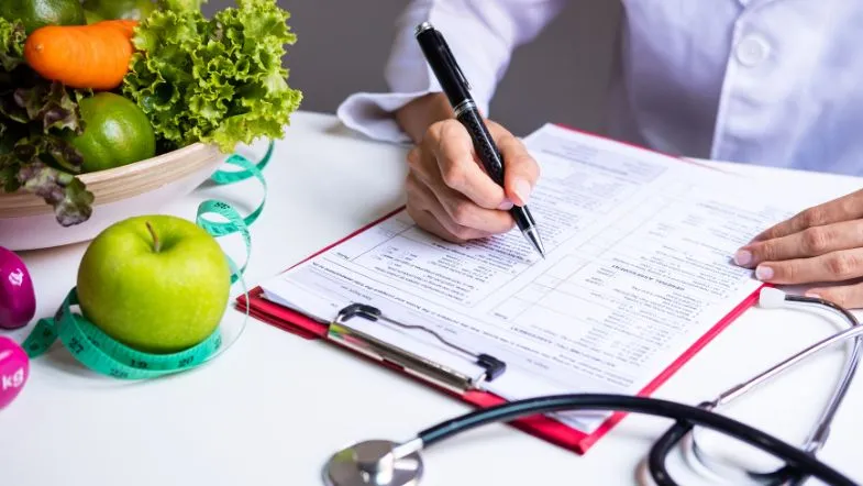 Profissional da Nutrição preenche ficha nutricional ao lado de alimentos e instrumentos de avaliação nutricional.