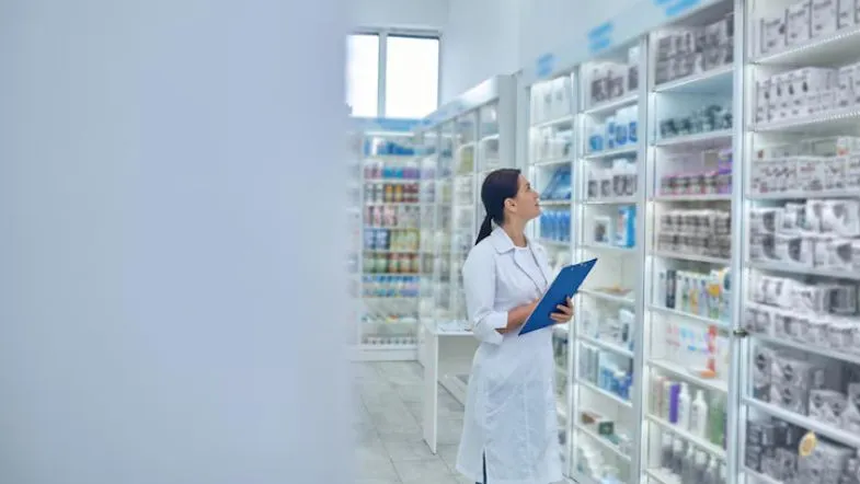 Especialização em Farmácia Hospitalar: descubra como se destacar no mercado da saúde 6 Profissional da farmácia hospitalar analisando estoque de medicamentos em prateleiras iluminadas, exemplificando controle e gestão de insumos.