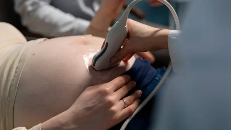 Profissional da saúde realizando exame de ultrassom em gestante durante o pré-natal, com foco na barriga e aparelho de imagem.