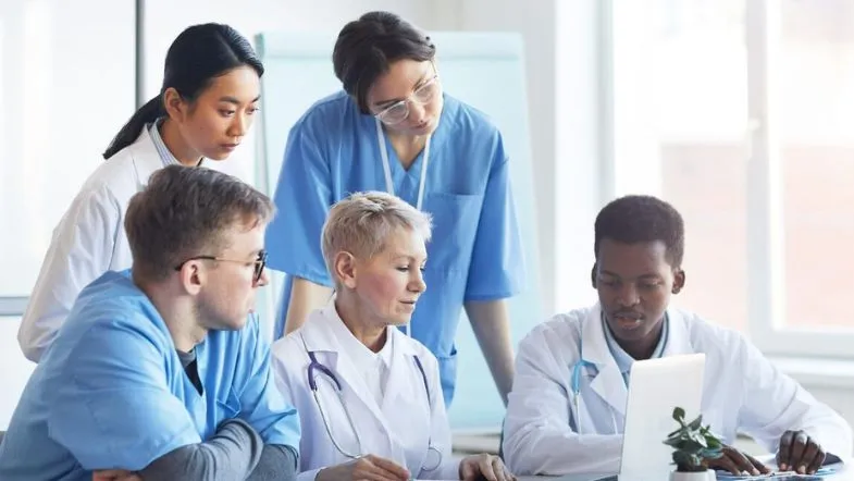 Gestão em Saúde: como o MBA transforma carreiras na área 7 Grupo de profissionais de enfermagem e médicos discutindo relatórios clínicos em frente ao laptop, reforçando o trabalho em equipe e gestão hospitalar.