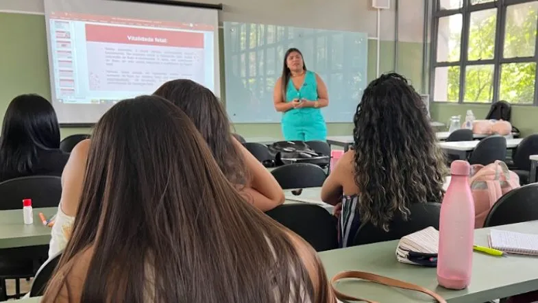 Educação de verdade: como a Faculdade ITH se prepara para os próximos 10 anos 7 Professora ministrando conteúdo em sala de aula com slides projetados, enquanto alunas acompanham atentamente e fazem anotações.