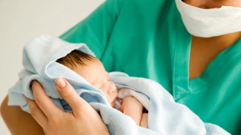 Atuação da enfermeira obstetra no parto humanizado: o que você precisa saber 7 Enfermeira obstetra segurando um recém-nascido envolvido em manta azul, logo após o nascimento.