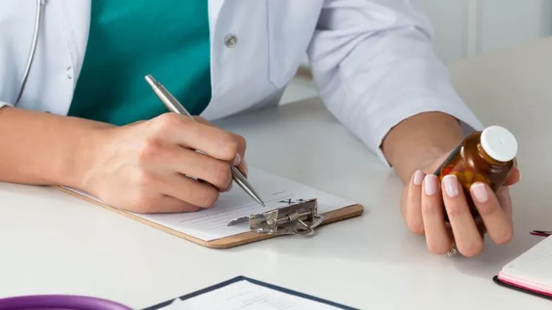 Farmacêutico prescrevendo medicamentos com frasco na mão durante atendimento clínico.