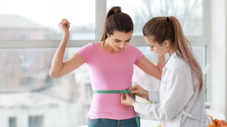 Nutricionista mede a circunferência da cintura de uma paciente com fita métrica em consultório.