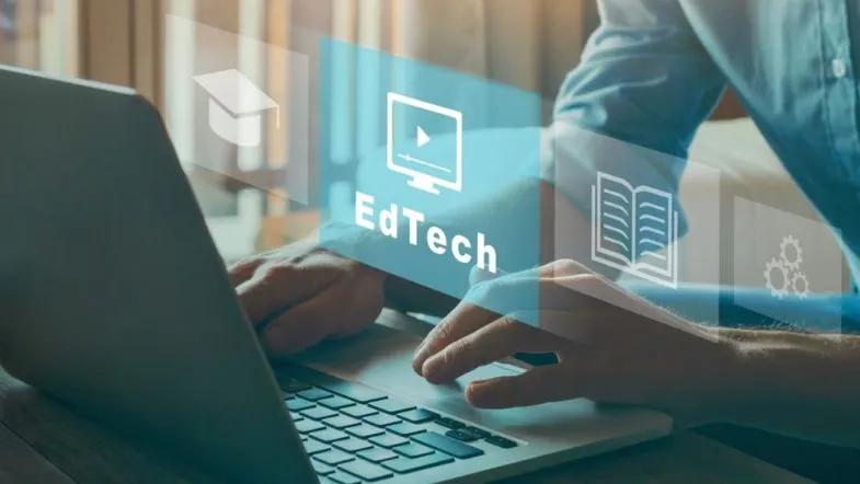 Edtechs: o que são e por que estão transformando a educação? 7 Pessoa digitando em laptop com interface digital holográfica com ícones de EdTech, vídeo, leitura e automação.